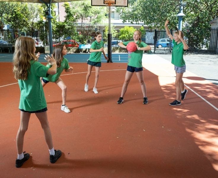 Five students playing netball on terracotta court