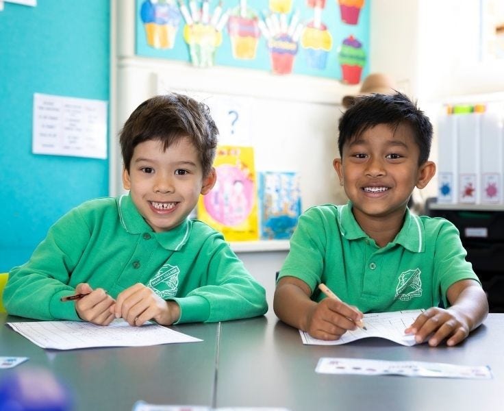 Two boys in green school polo shirts smiling at camera with pencils in hand